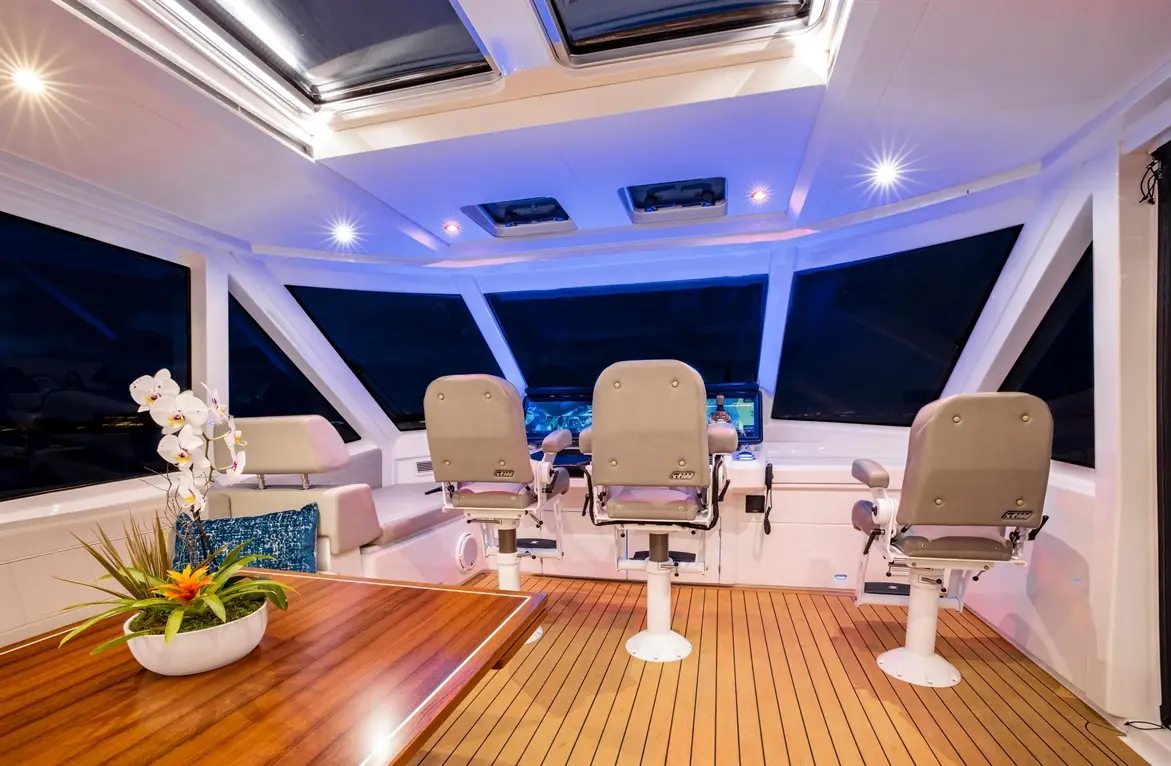 Modern boat cockpit featuring grey captain's chairs, a wooden table, and decorative plants under warm LED lighting.